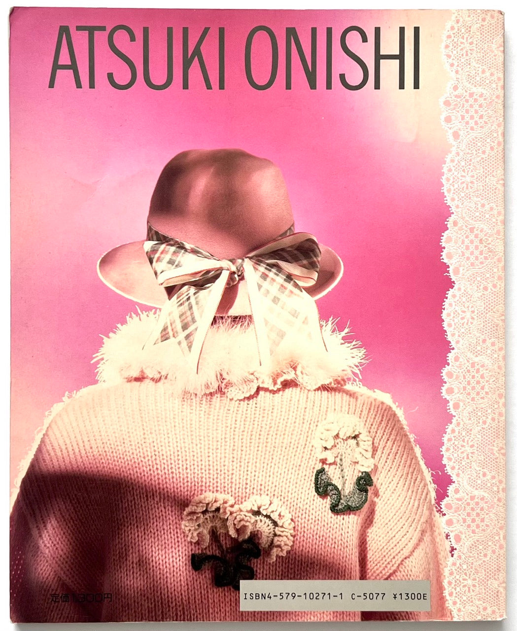Back cover of Atsuki Onishi no Knit Ehon (Atsuki Onishi's Knit Picture Book) by Atsuki Onishi, published in 1989, featuring the rear view of a model in a pink knit sweater with floral appliqués and a ribbon-trimmed pink hat, set against a bright pink background with lace border detailing.