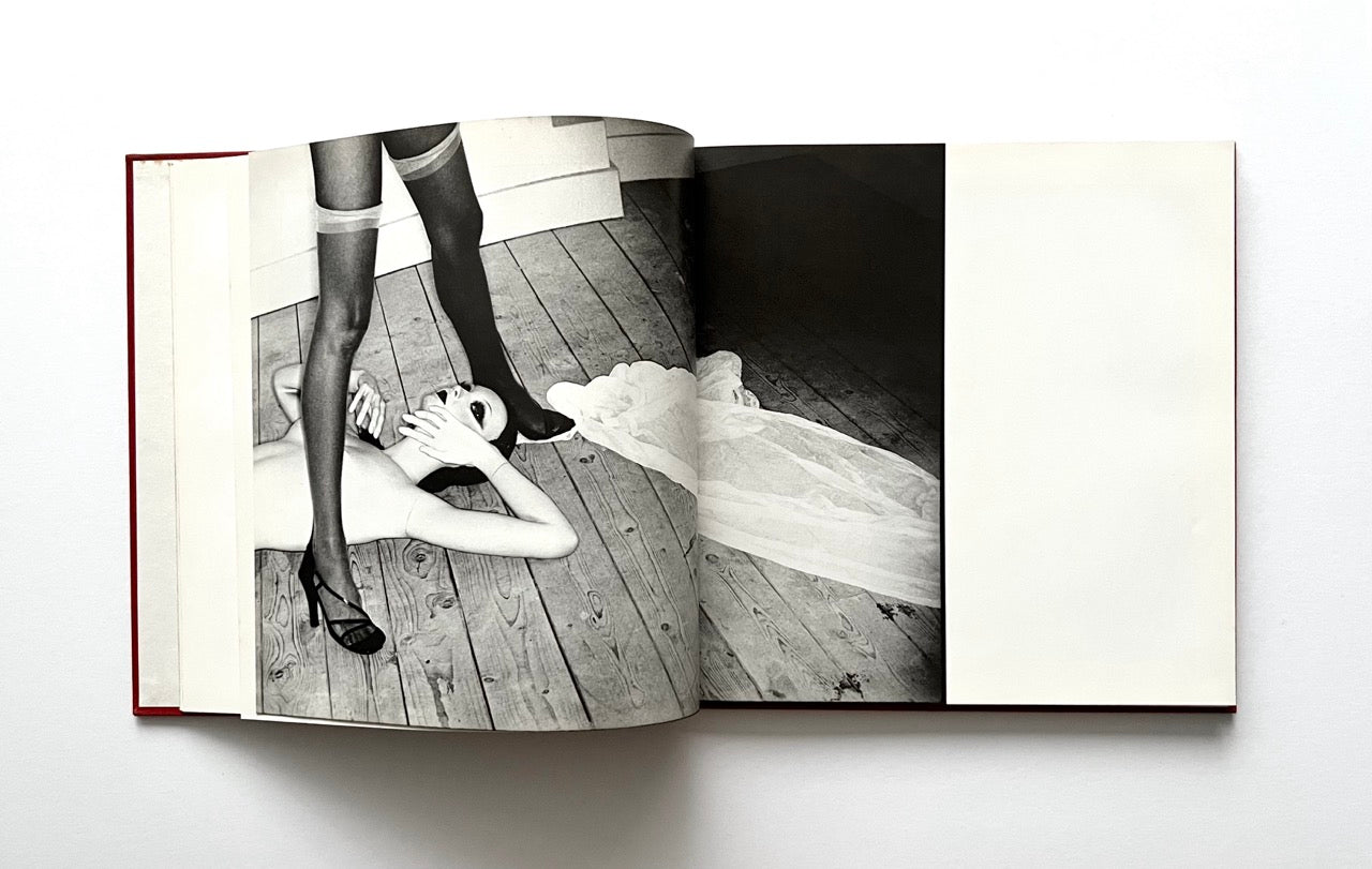 Open David Bailey's Trouble and Strife' book with a black and white photograph of nude Marie Helvin and a woman in high heels and stockings, and a dress on a wooden floor.