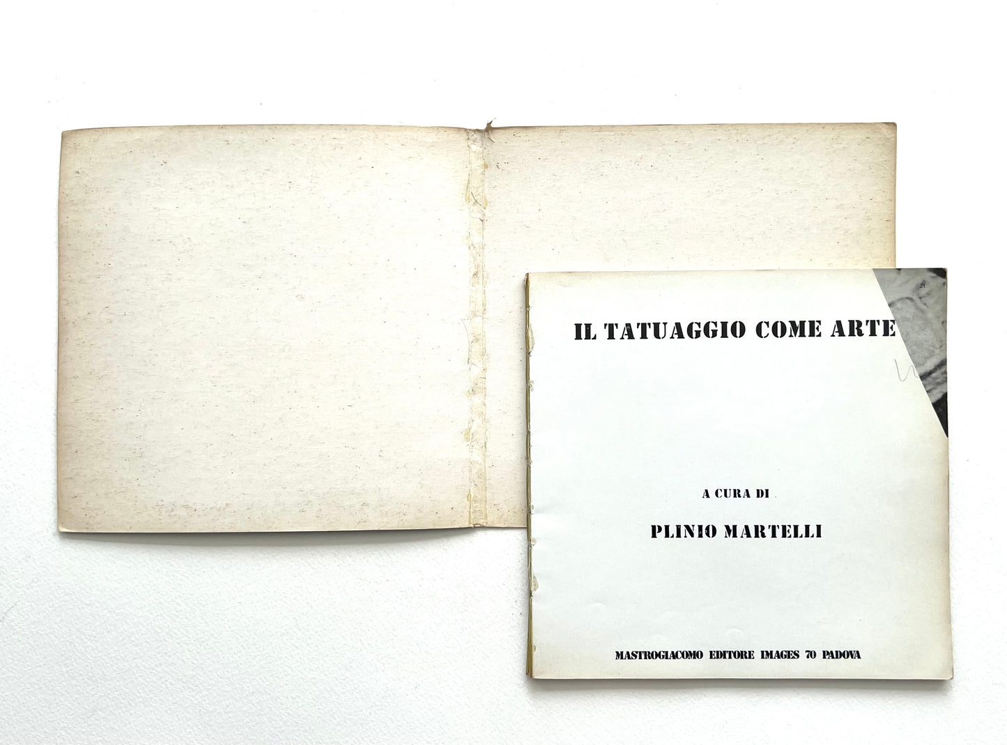 Open book with a cover titled 'Il Tatuaggio Come Arte' by Plinio Martelli on a white background