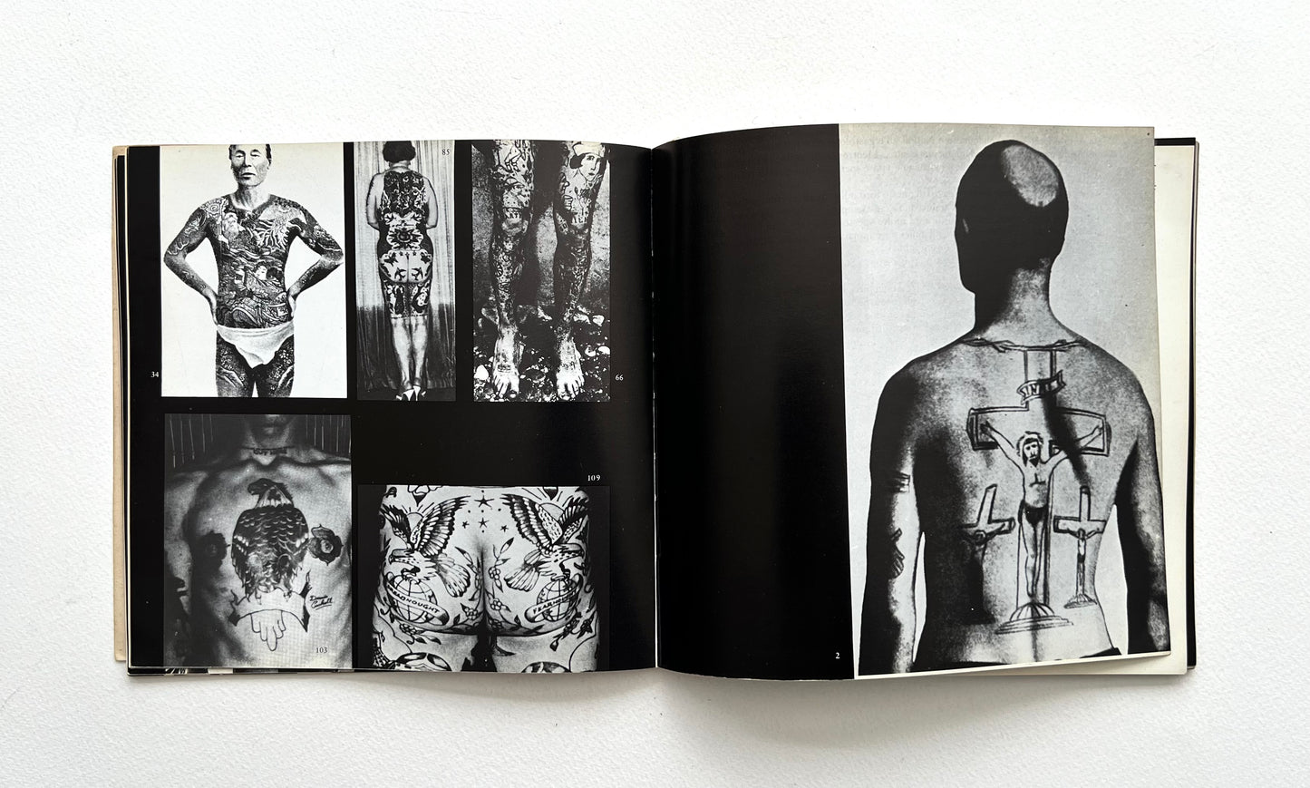 Open book showing black and white images of tattoos on body parts on a white background