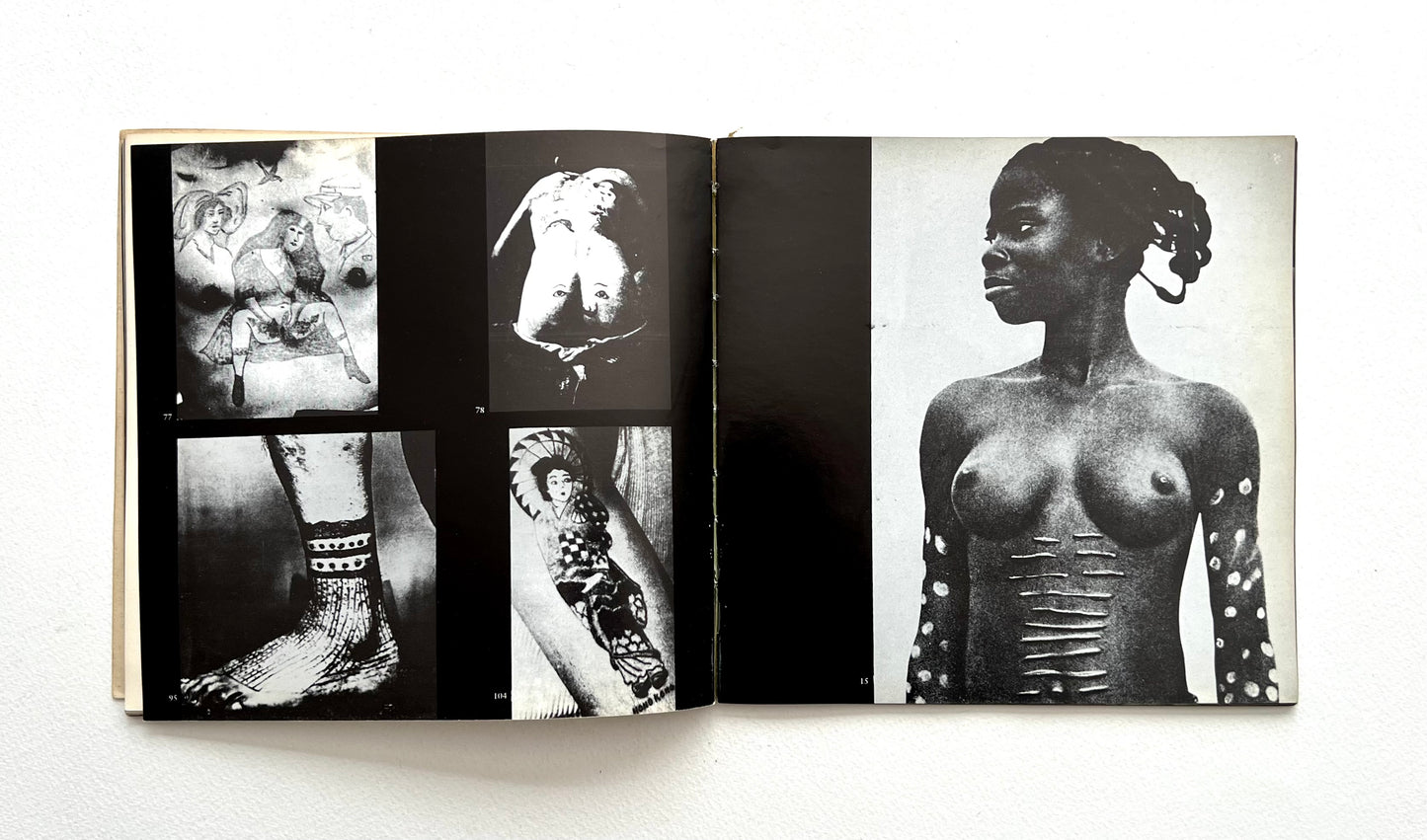 Open book displaying black and white photographs of a woman with tattoos on a white background