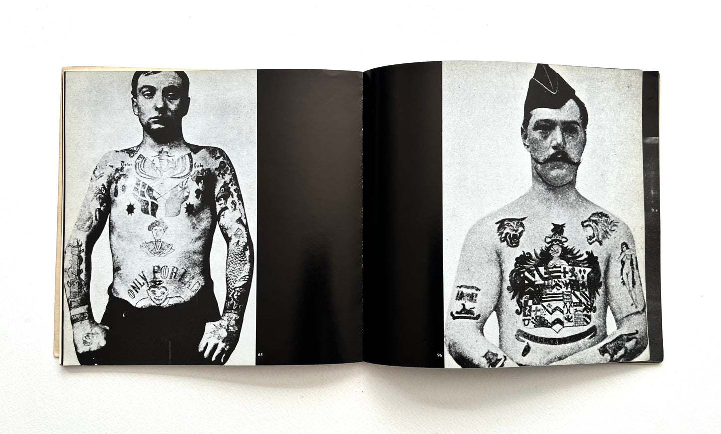 Open book showing black and white photographs of men with tattoos on a white background