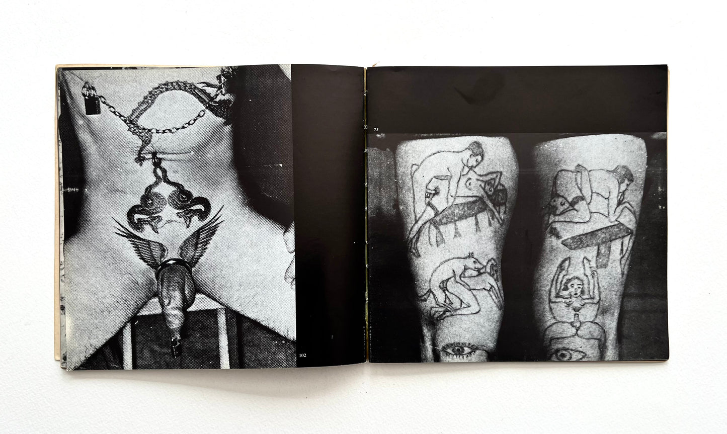 Open book showing black and white images of tattoos on stomach and legs on a white background
