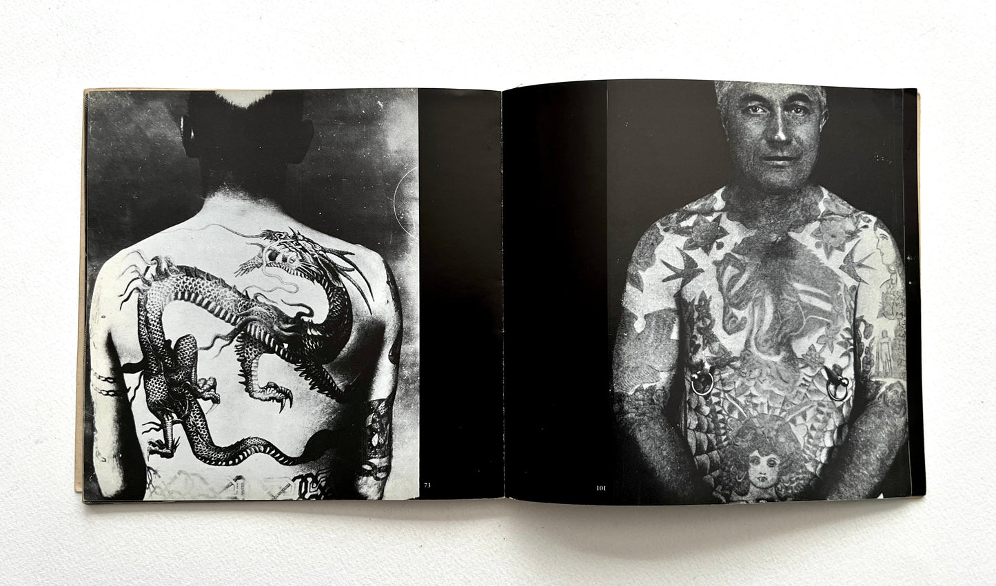 Open book showing black and white images of tattoos on a person's back, torso and arms.