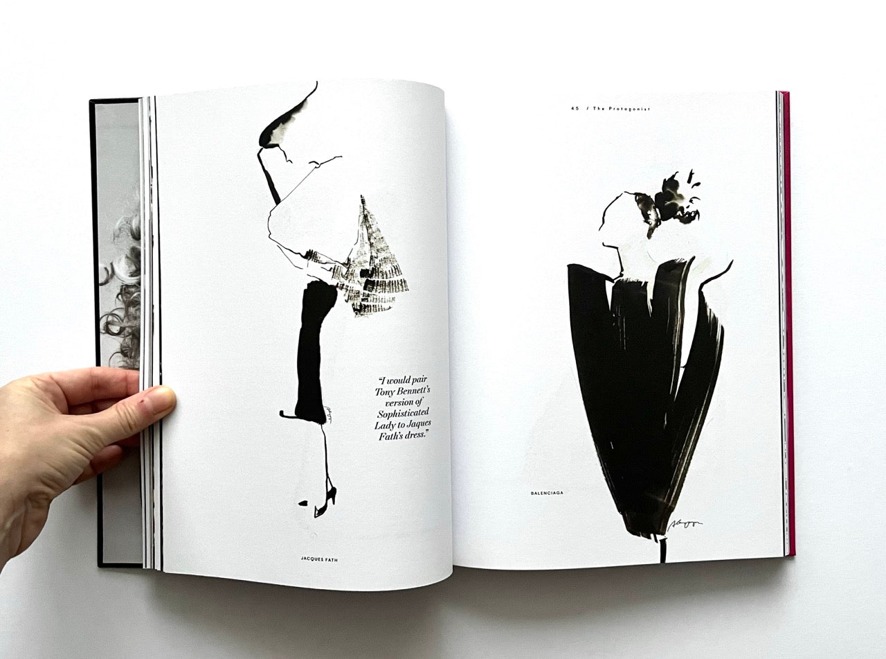 Open 'The Protagonist Magazine' issue 2, with black and white fashion sketches, held by a hand on a white background.