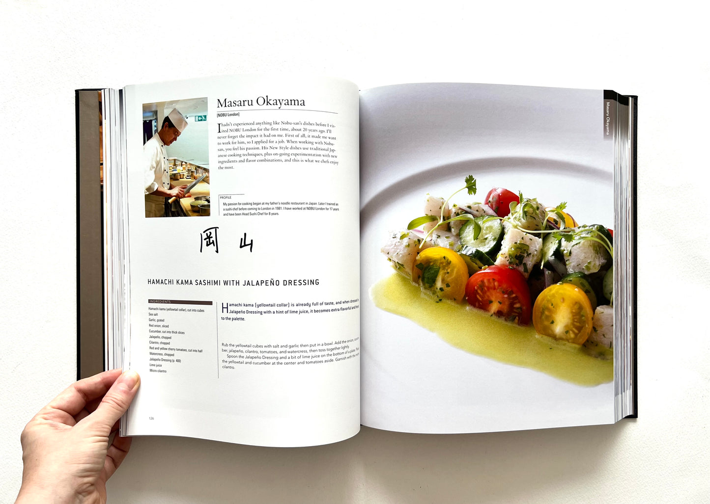 Open 'World of Nobu" cookbook showing a page with a recipe and a photograph of HAMACHI KAMA SASHIMI WITH JALAPEÑO DRESSING dish - singed by Masaru Okayama.
