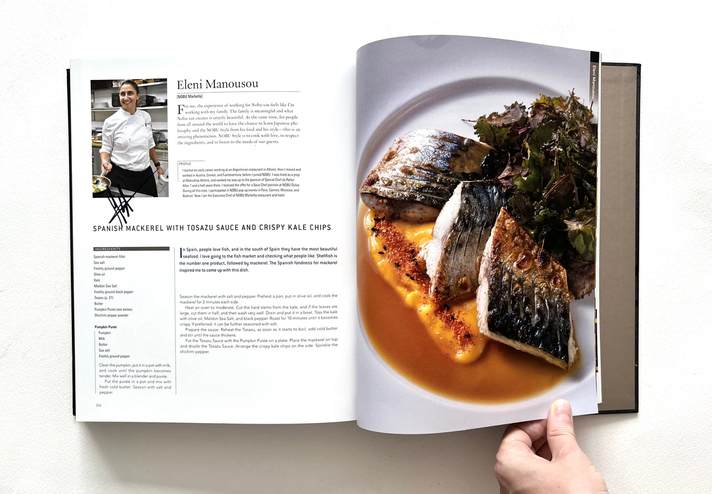 Open "Wordl of Nobu" cookbook showing a recipe and a photo of a SPANISH MACKEREL WITH TOSAZU SAUCE AND CRISPY KALE CHIPS dish - signed by chef Eleni Manousou.