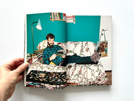 Apartamento Magazine Issue #21 – Interior spread showing a man reclining on a patterned sofa in a colourful living room, reading a magazine with eclectic decor.