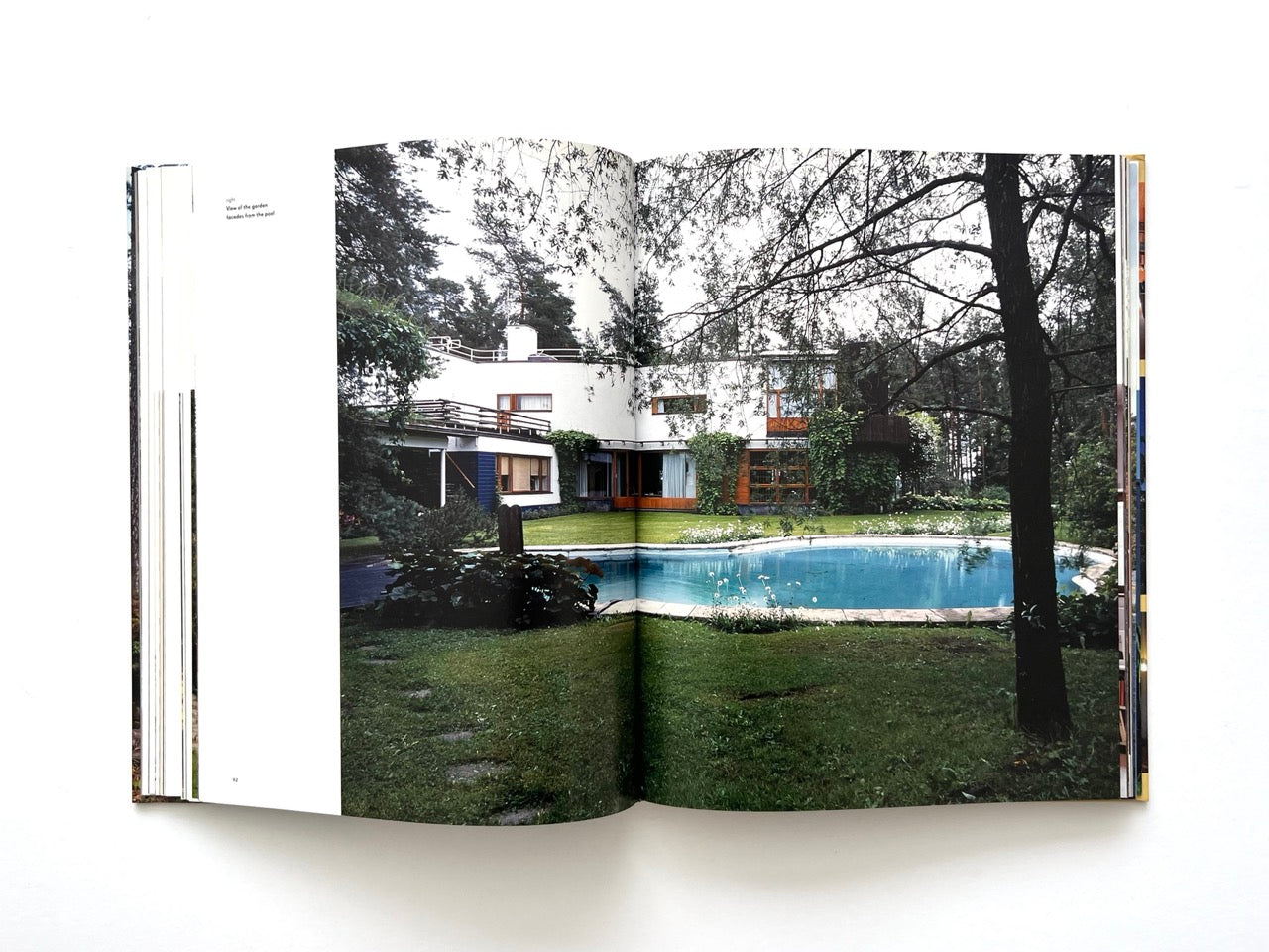 Double-page photograph from Alvar Aalto Houses (2011) by Jari Jetsonen and Sirkkaliisa Jetsonen, featuring Villa Mairea with its landscaped garden, swimming pool and modernist architecture surrounded by woodland.