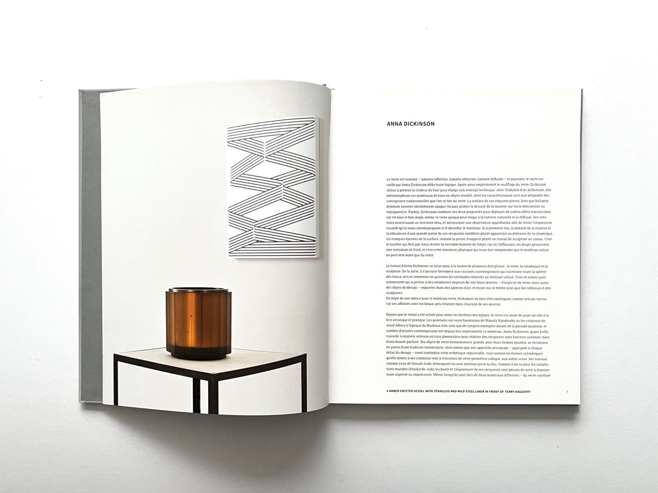Open spread of the book “Anna Dickinson”, showing a sculptural amber glass vessel displayed on a small table beneath a geometric line artwork on the left page and an essay text layout on the right page, against a white background.