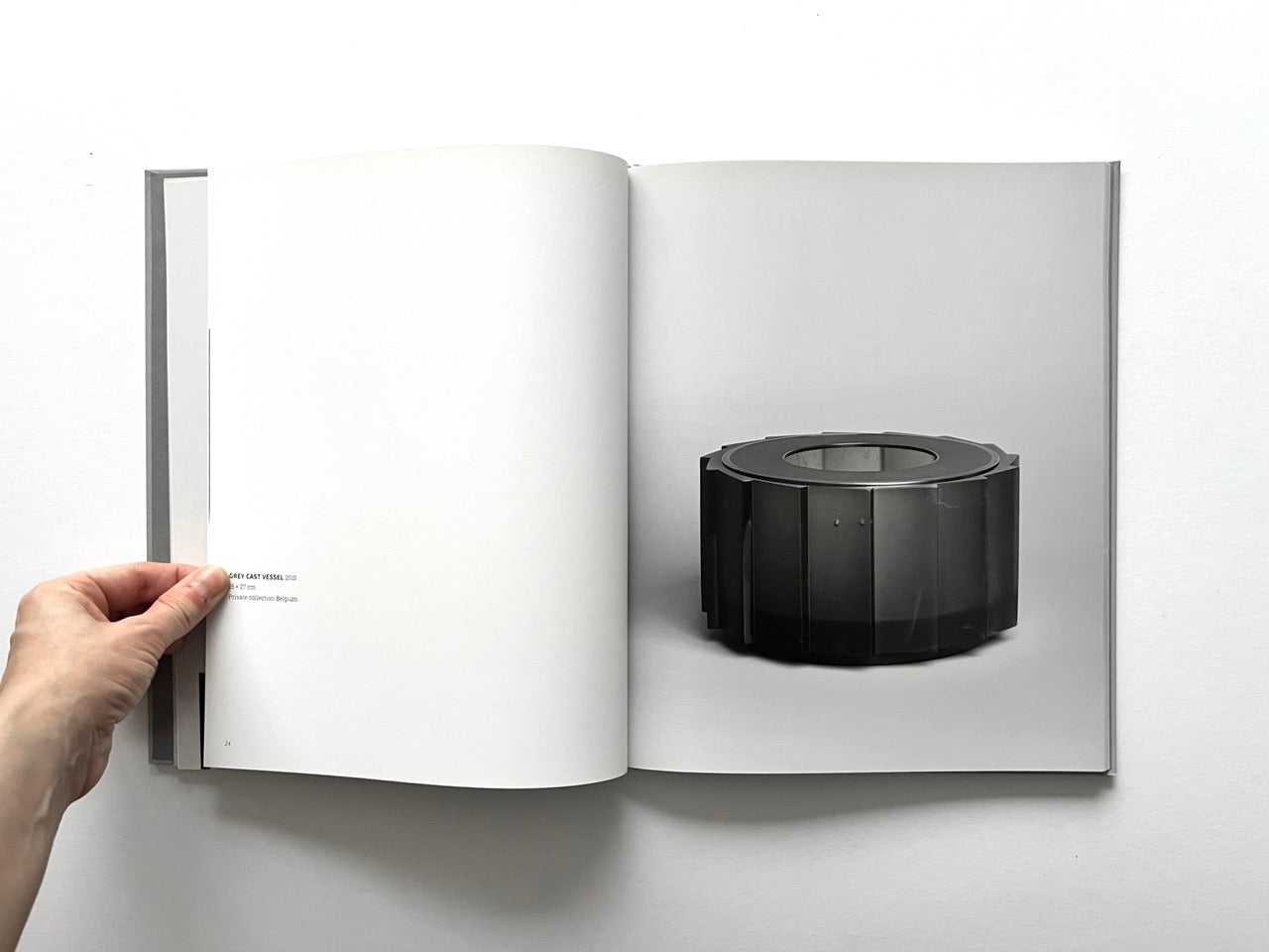 Open spread of the book “Anna Dickinson”, showing a full-page photograph of a dark grey cast glass vessel with a segmented circular form on the right page, against a neutral grey background.