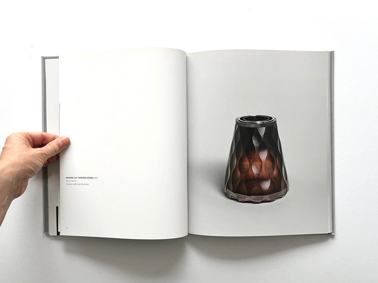 Open spread of the book “Anna Dickinson”, showing a full-page photograph of a faceted brown glass vessel with a tapered form and dark rim on the right page, against a neutral grey background.