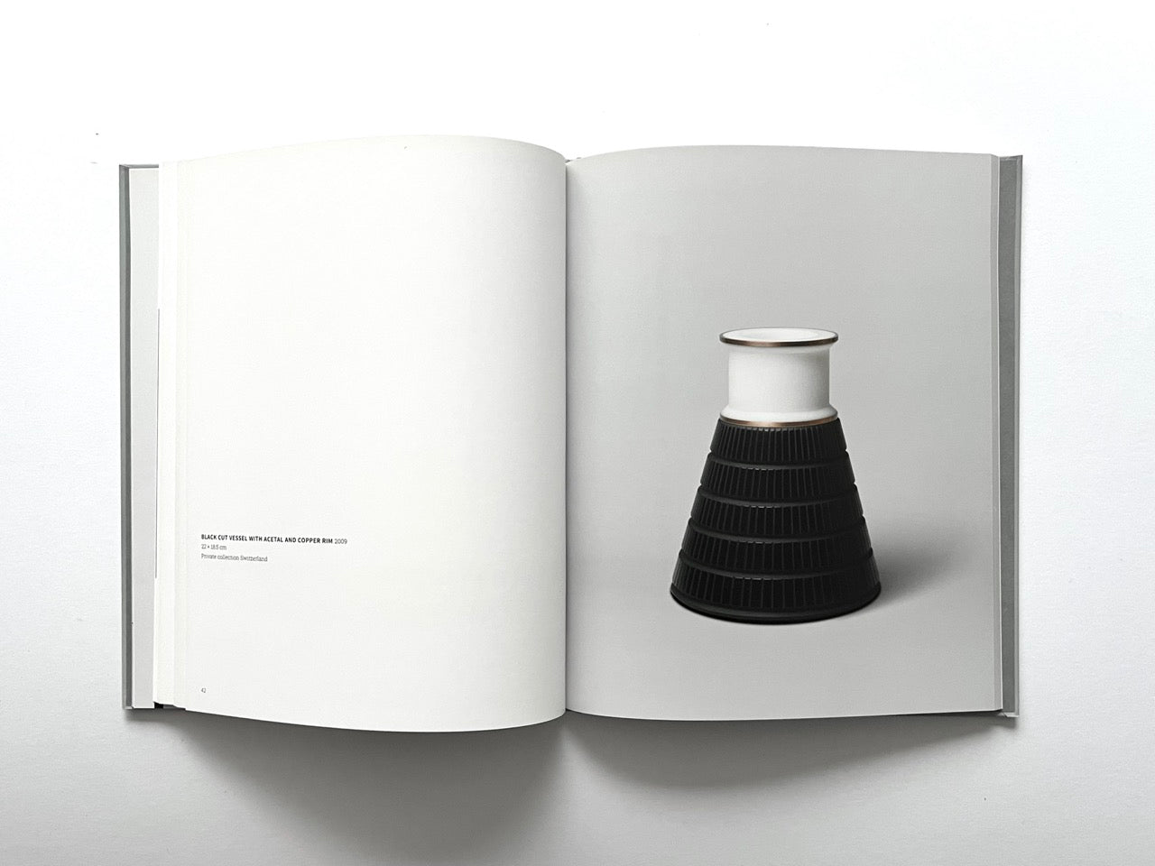 Open spread of the book “Anna Dickinson”, showing a full-page photograph of a black tapered glass vessel with a white upper section and metallic rim on the right page, against a neutral grey background.