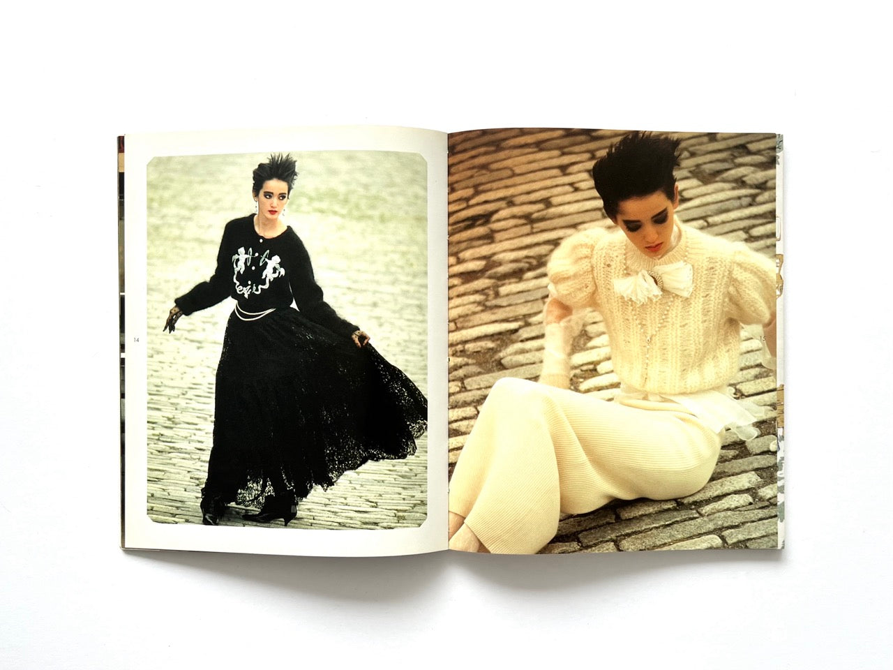 Interior spread from Atsuki Onishi's Knit Picture Book, published in 1989, featuring contrasting black and ivory knit outfits photographed on cobbled streets in an editorial fashion shoot.