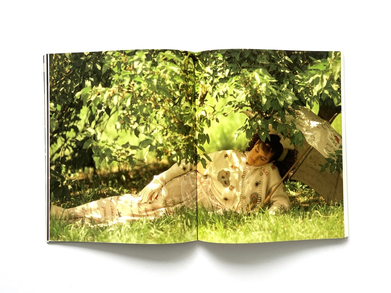 Interior spread from Atsuki Onishi's Knit Picture Book, published in 1989, showing a fashion model reclining beneath leafy trees while wearing embroidered knitwear and holding a decorative parasol.