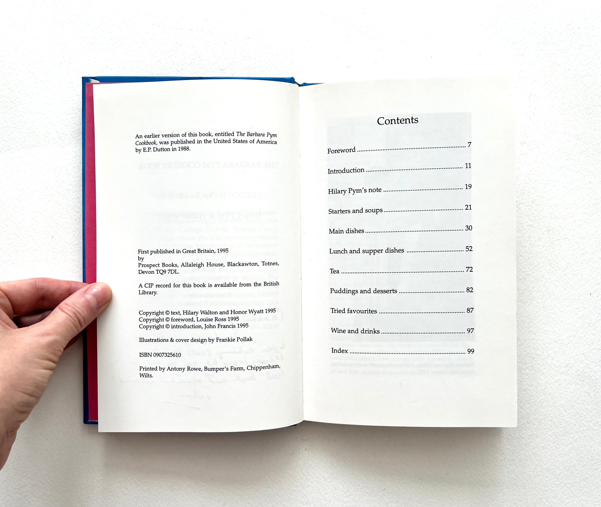 Open book showing a table of contents of 'A la Pym\ cookery book held by a hand on a white surface