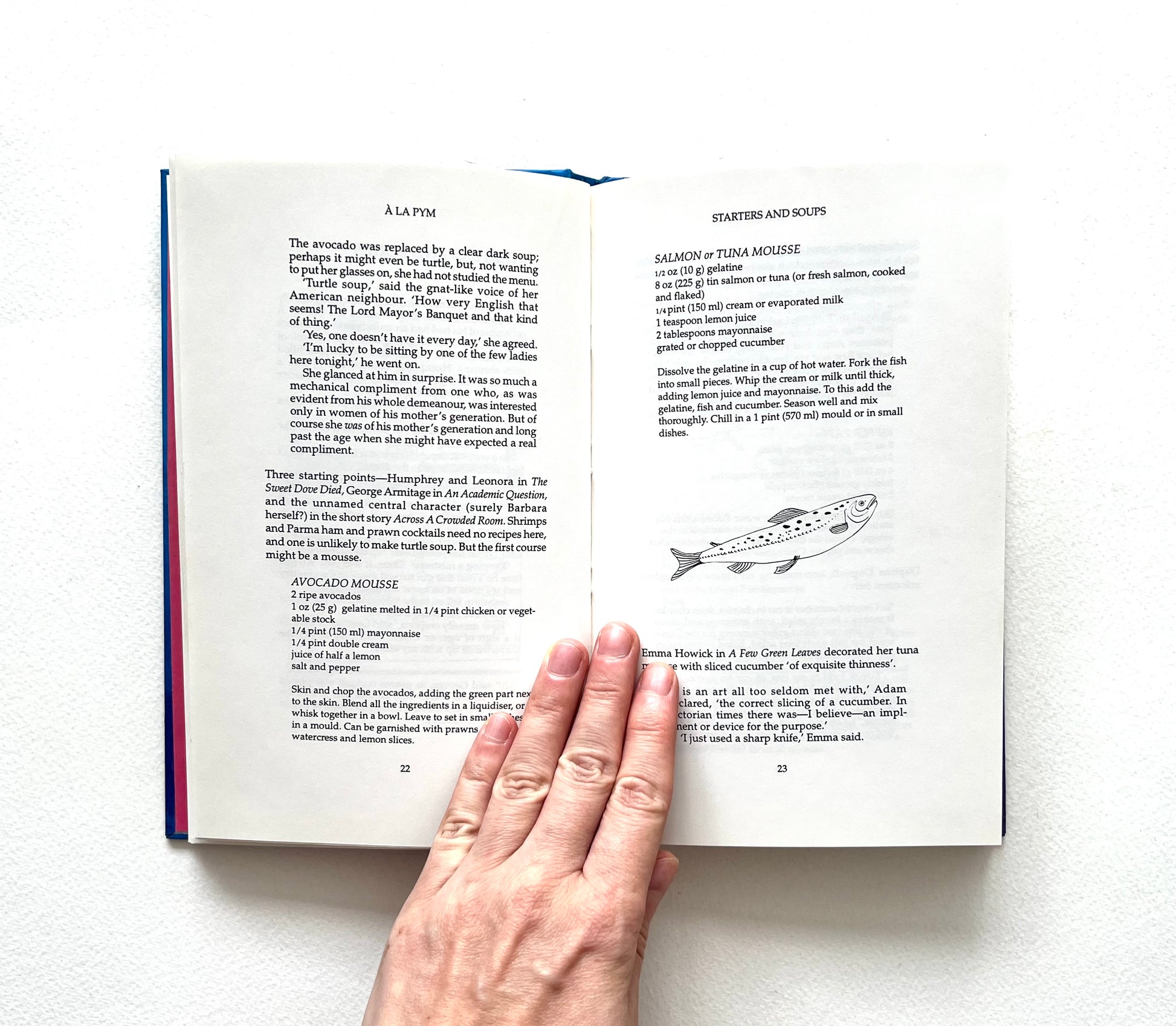 Open book with text and a line drawing of a fish on a white background, held open by a hand.