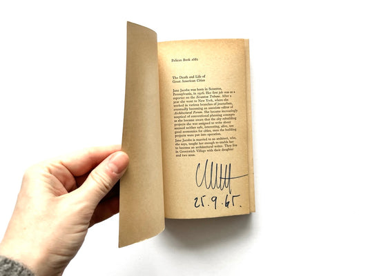 Interior title page of The Death and Life of Great American Cities by Jane Jacobs, Pelican Book edition, showing aged paper, printed author biography text, and a handwritten signature with a date at the bottom of the page.