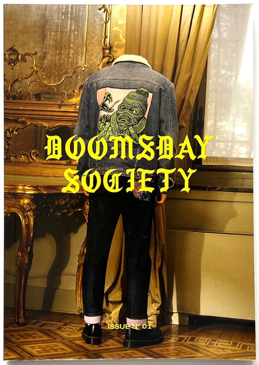 Doomsday Society Issue No. 01 – Cover showing a figure in a denim jacket with graphic illustration on the back, standing in an ornate interior with bold gothic yellow title text.