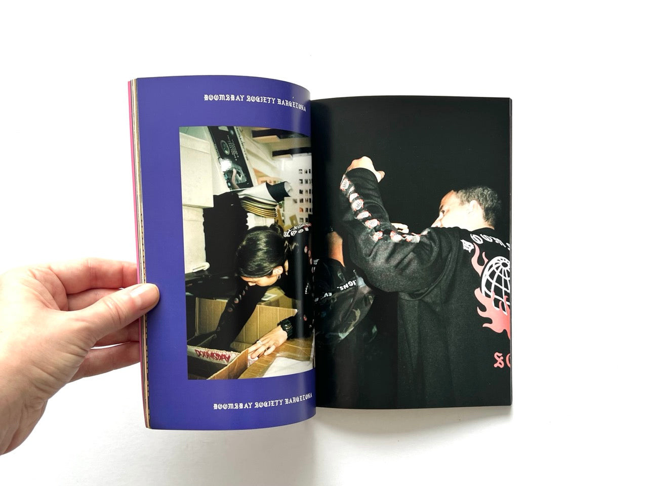 Doomsday Society Issue No. 01 – Interior spread showing behind-the-scenes scene of packing garments and a figure in black jacket with flame graphic and logo.