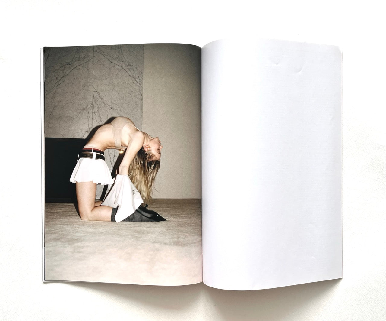 Open magazine showing a Sydney Sweeney in a white mini skirt with a black belt in a minimalist setting.