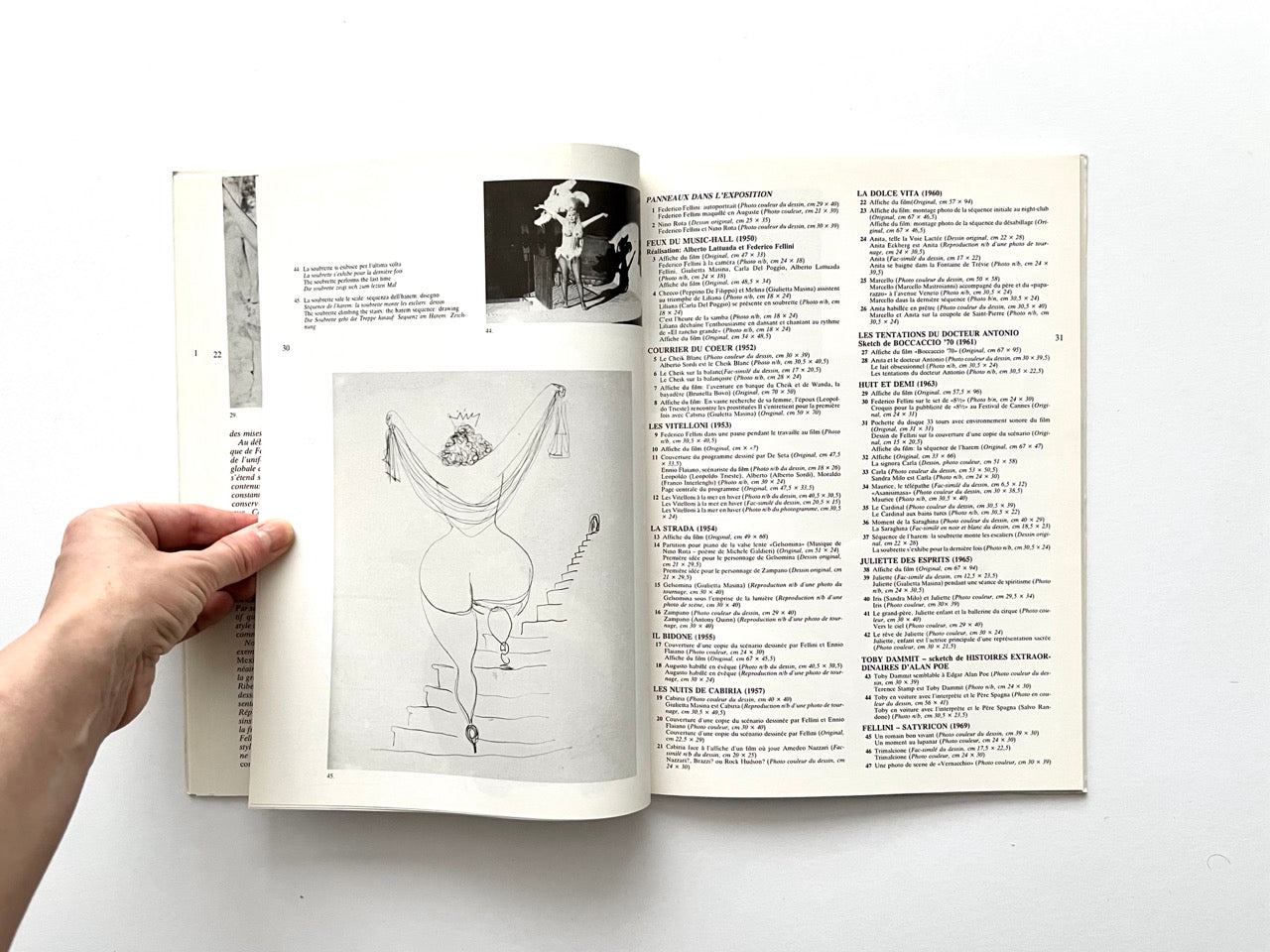 Interior spread with a pencil drawing of a woman descending a staircase, viewed from behind, on the left page. Right page contains a list of Fellini’s films and works shown in the exhibition, printed in multiple columns. A small black-and-white photograph of a costumed performer appears above.