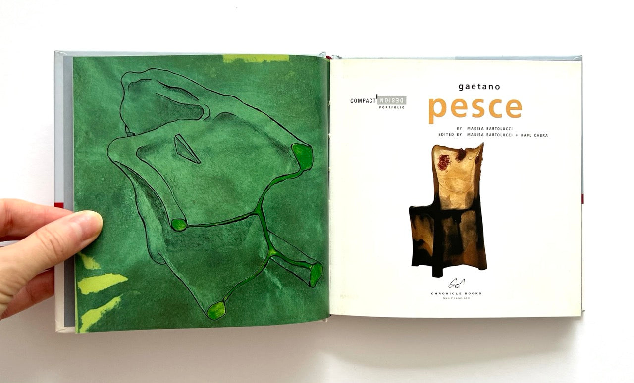Open book - GAETANO PESCE
by Marisa Bartoluccii - with a green abstract drawing on one page and text on the other, held by a hand.