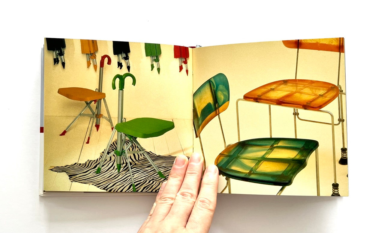 Open book - GAETANO PESCE
by Marisa Bartolucci - showing colourful modern chairs and a hand turning the page.