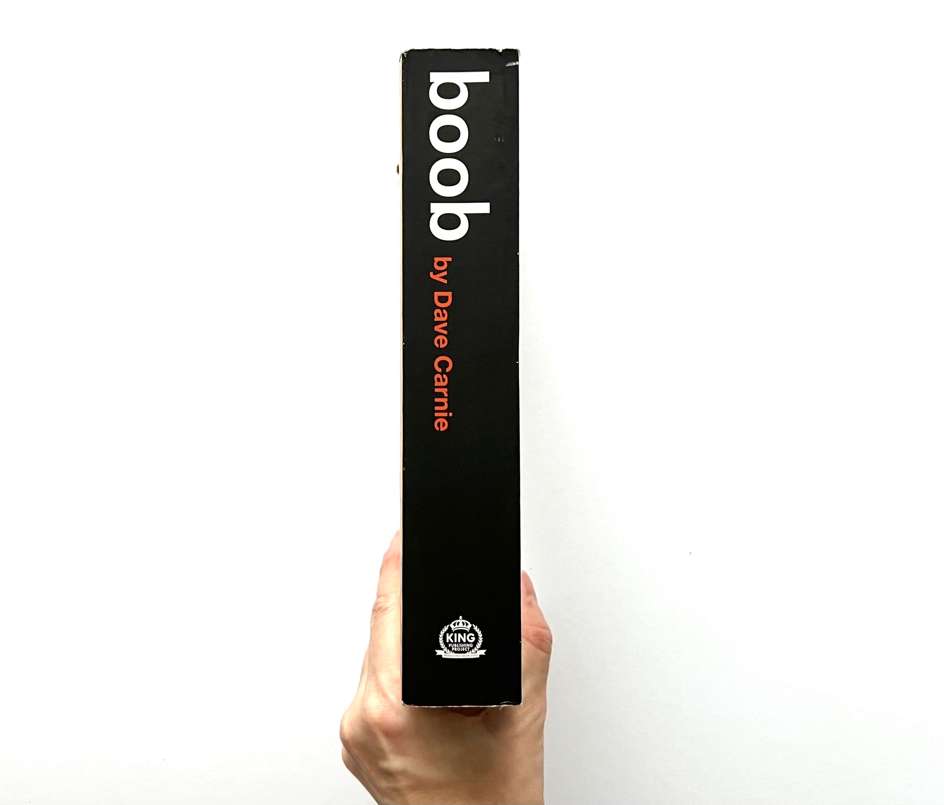 Close-up of the book spine for “boob” by Dave Carnie, held upright by a hand against a white background.