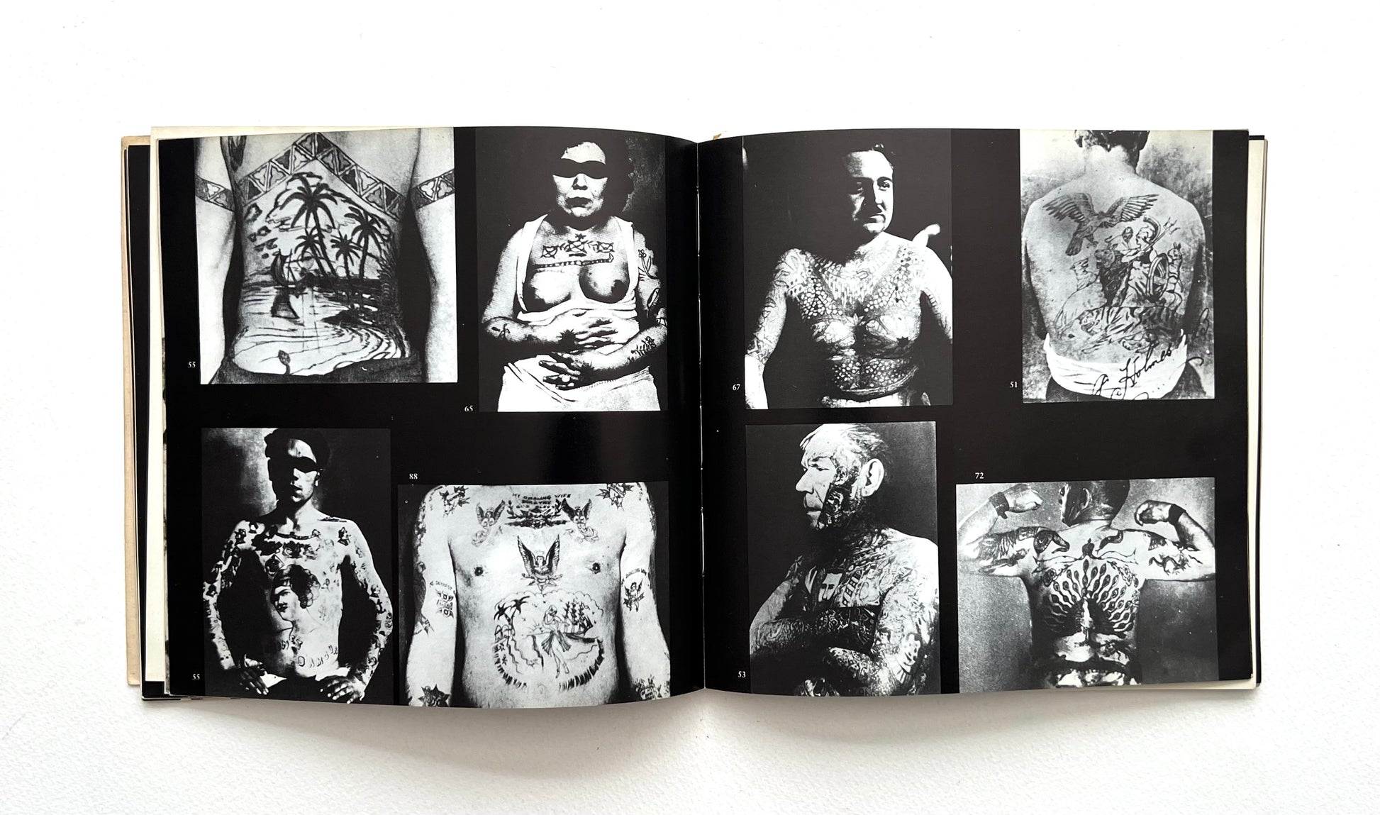 Open book displaying black and white images of tattoos on people's bodies.