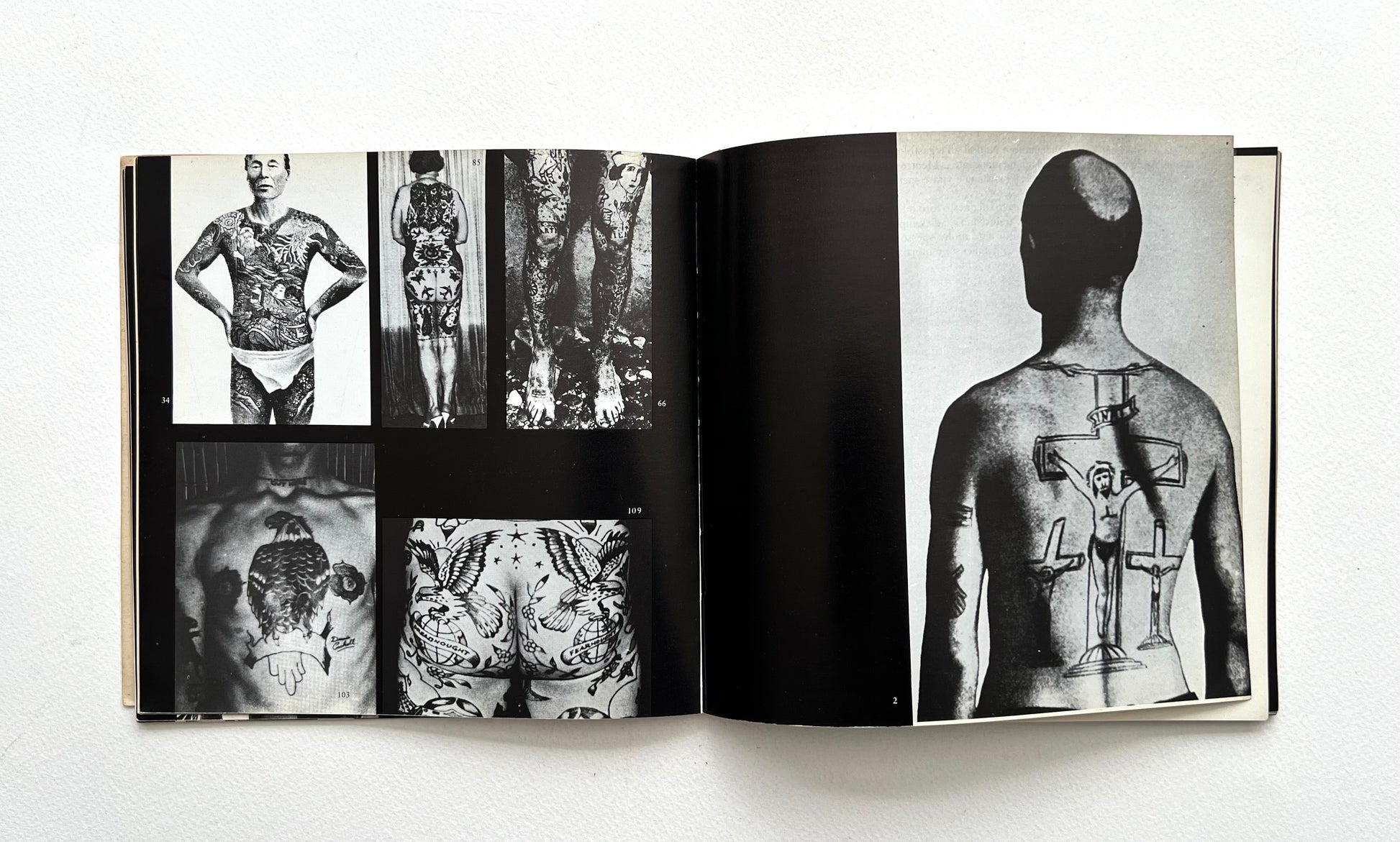 Open book showing black and white images of tattoos on body parts on a white background