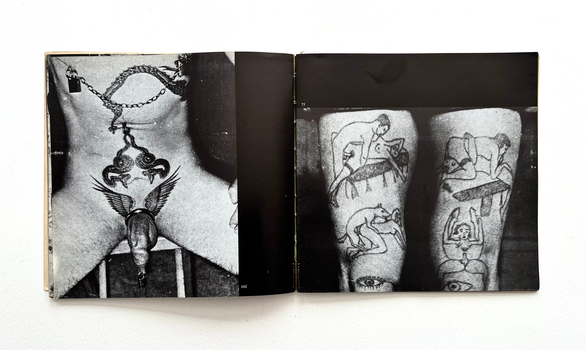 Open book showing black and white images of tattoos on stomach and legs on a white background