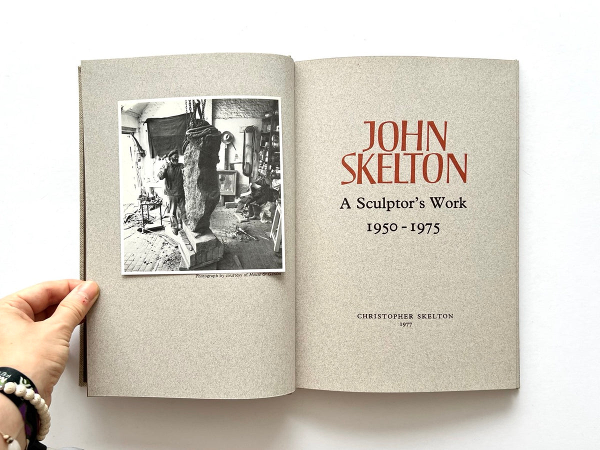 John Skelton: A Sculptor’s Work 1950–1975 (1977). Interior title spread with a black-and-white photograph of John Skelton working in his studio beside a large stone sculpture on the left, and the title page in red and black typography on the right.