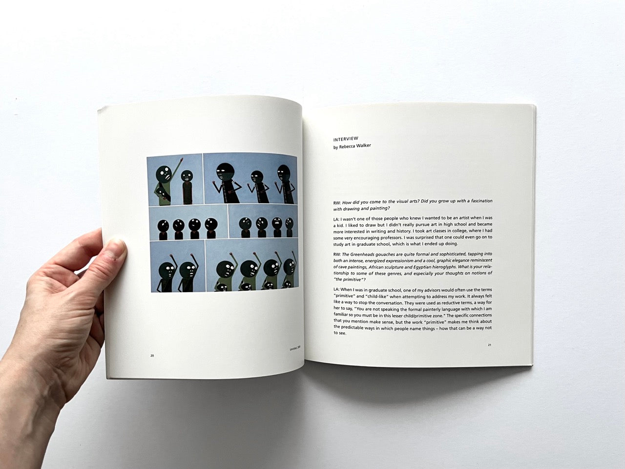 Open spread of the book “Laylah Ali”, showing a grid of small figurative painting reproductions with stylised human figures on the left page and an interview text layout on the right page, held open by a hand against a white background.
