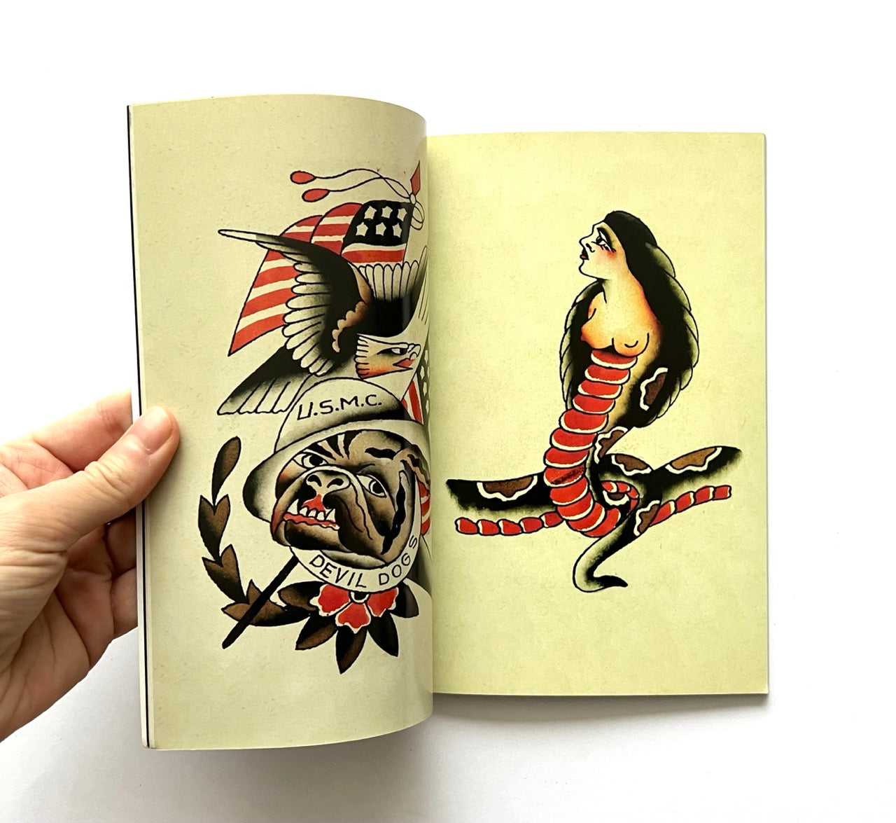 Open book - 'LOST ART: FROM TATTOOING’S PAST' - displaying vintage tattoo designs: an eagle, American flag, helmet, and snake on a beige background.