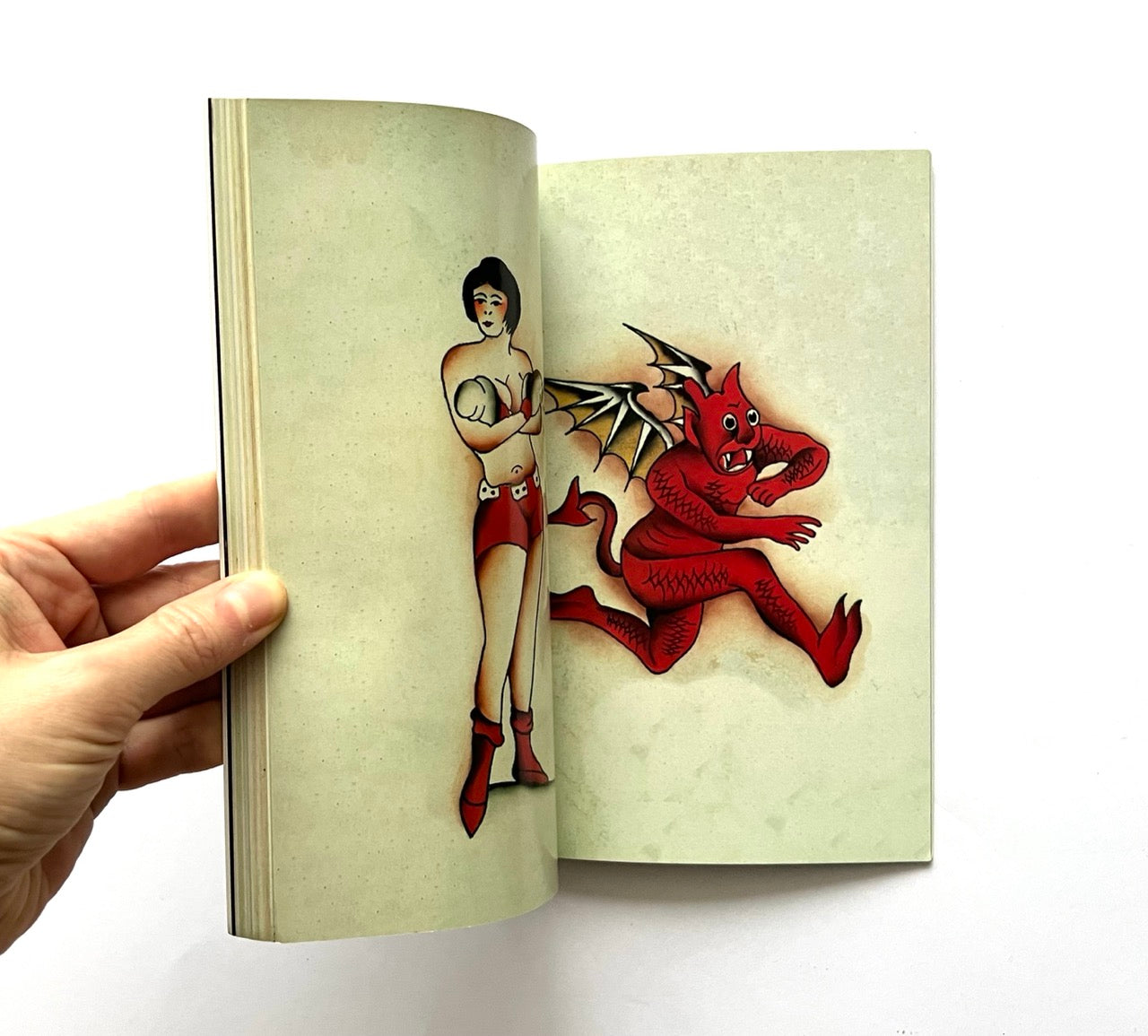 Open book - 'LOST ART: FROM TATTOOING’S PAST' - displaying vintage tattoo designs of a woman and a red devil on beige pages.