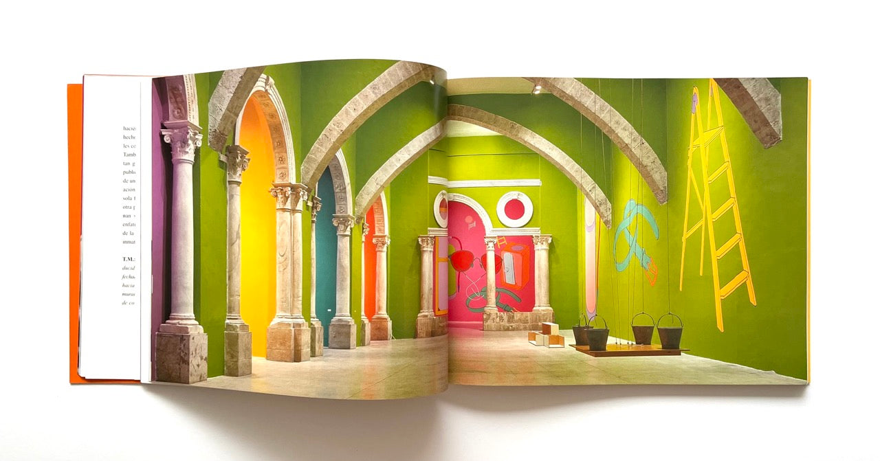 Open book showing a colorful gallery interior with stone arches and a ladder painted on the wall.