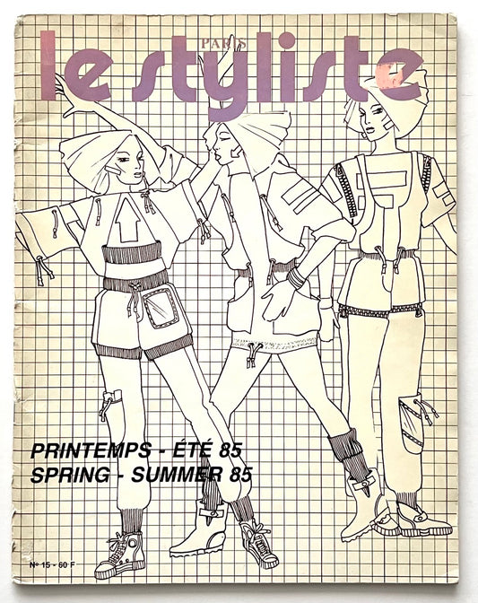 Front cover of Paris Le Styliste No 15 Spring–Summer 1985: cream grid background with three outlined fashion illustrations in sporty 80s silhouettes, oversized hoods and layered garments; bold lavender title at top; French/English season text printed in black at bottom.