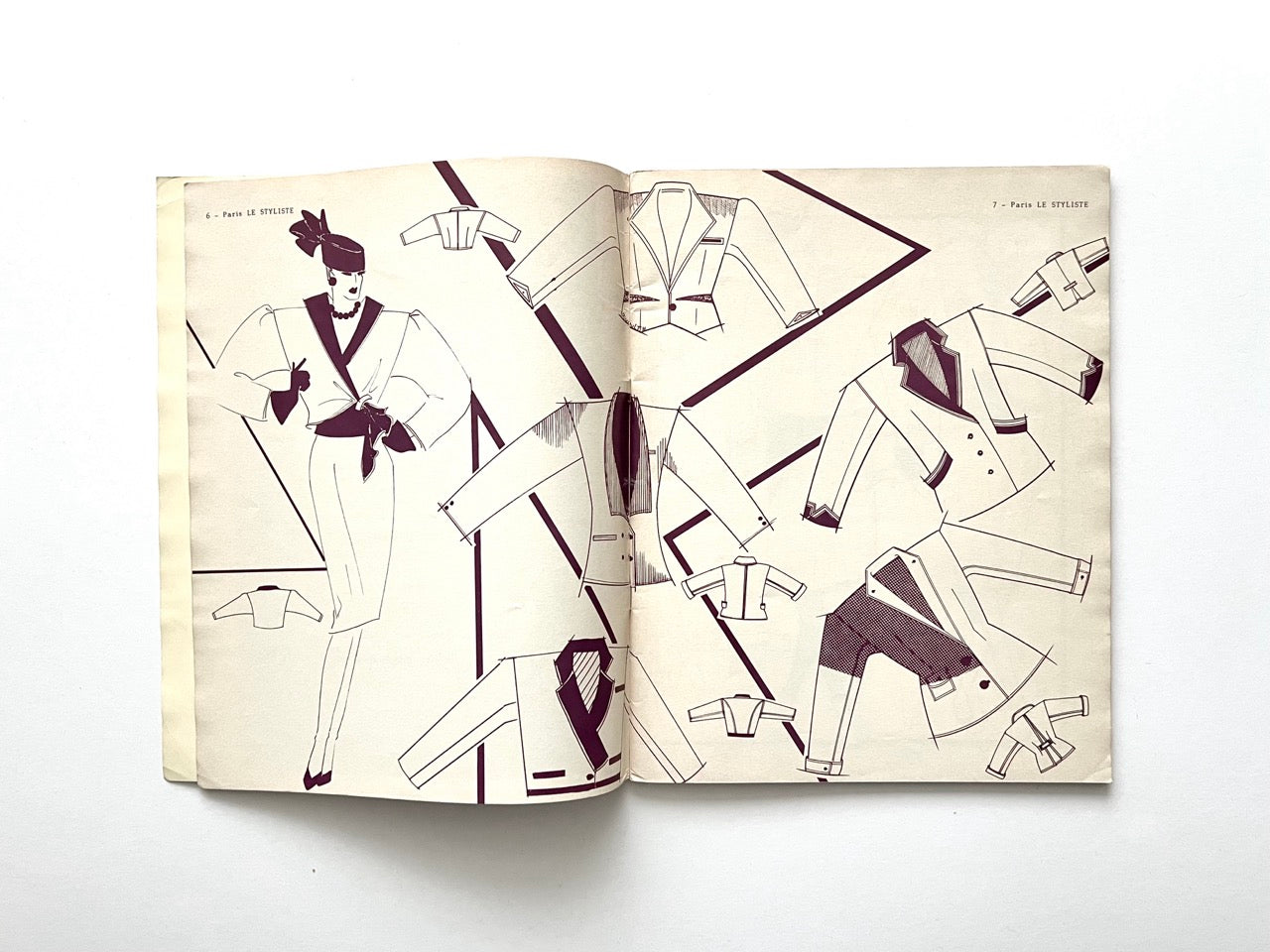 Interior spread from Paris Le Styliste No. 15 (1985) featuring line-drawn jacket and blazer designs; left page shows a stylised model in a belted suit with hat, right page displays multiple jacket variations arranged diagonally on a cream background.