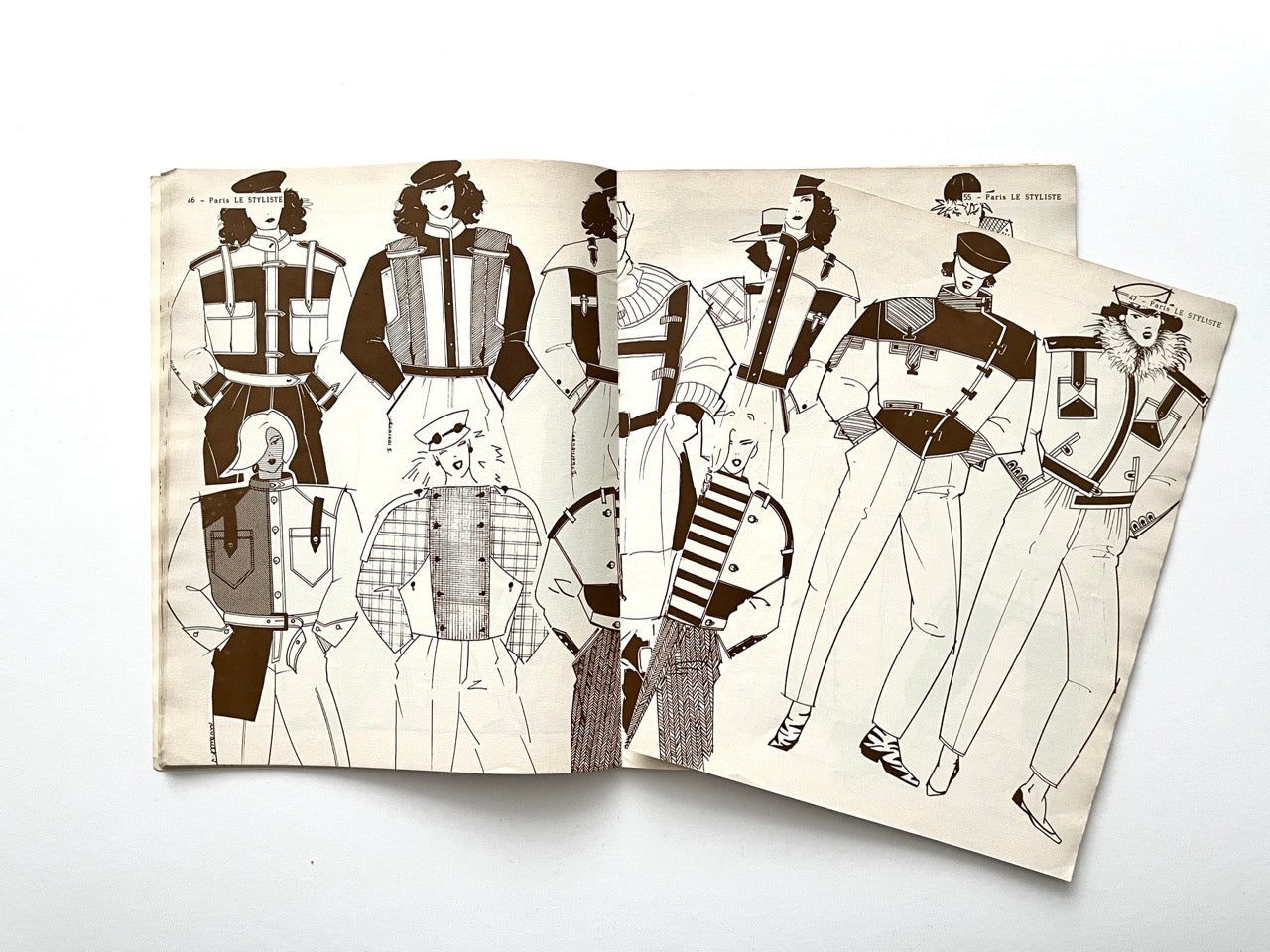 Illustrated spread featuring a mix of utility-style 1980s jackets with quilted panels, epaulettes, contrast pockets and bold geometric shapes; an extra loose sheet partially overlays the right page showing additional jacket designs.
