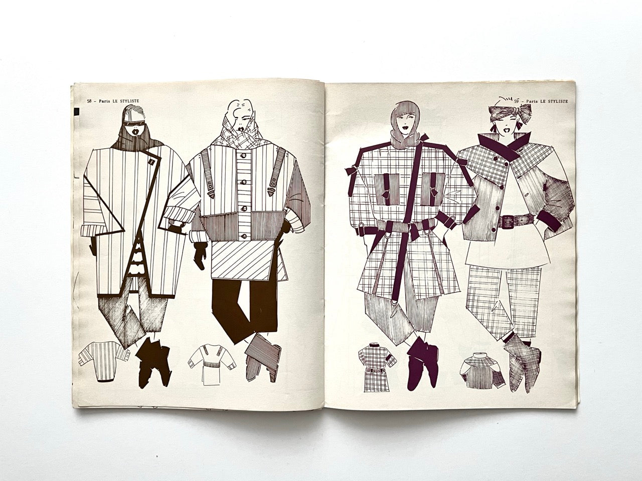 Spread from Paris Le Styliste No. 15 (1985) displaying four figures in oversized outerwear: long striped coats, belted plaid jackets and angular caped silhouettes, each accompanied by small technical drawings at the bottom.