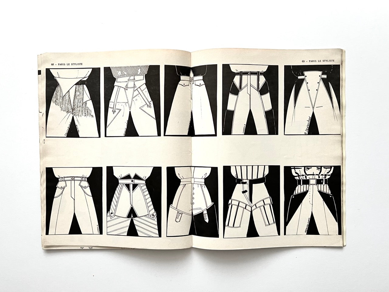 Two-page spread from Paris Le Styliste No. 15 (1985) displaying twelve close-up illustrations of trouser waistlines and hip constructions, each showing different pleats, overlaps, button placements and layered panels against black rectangles.