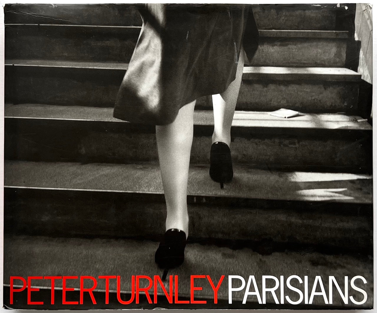 Front cover of Parisians by Peter Turnley, published in 2000, featuring a black-and-white street photograph of a woman ascending a staircase, with bold red and white typography across the bottom of the dust jacket.