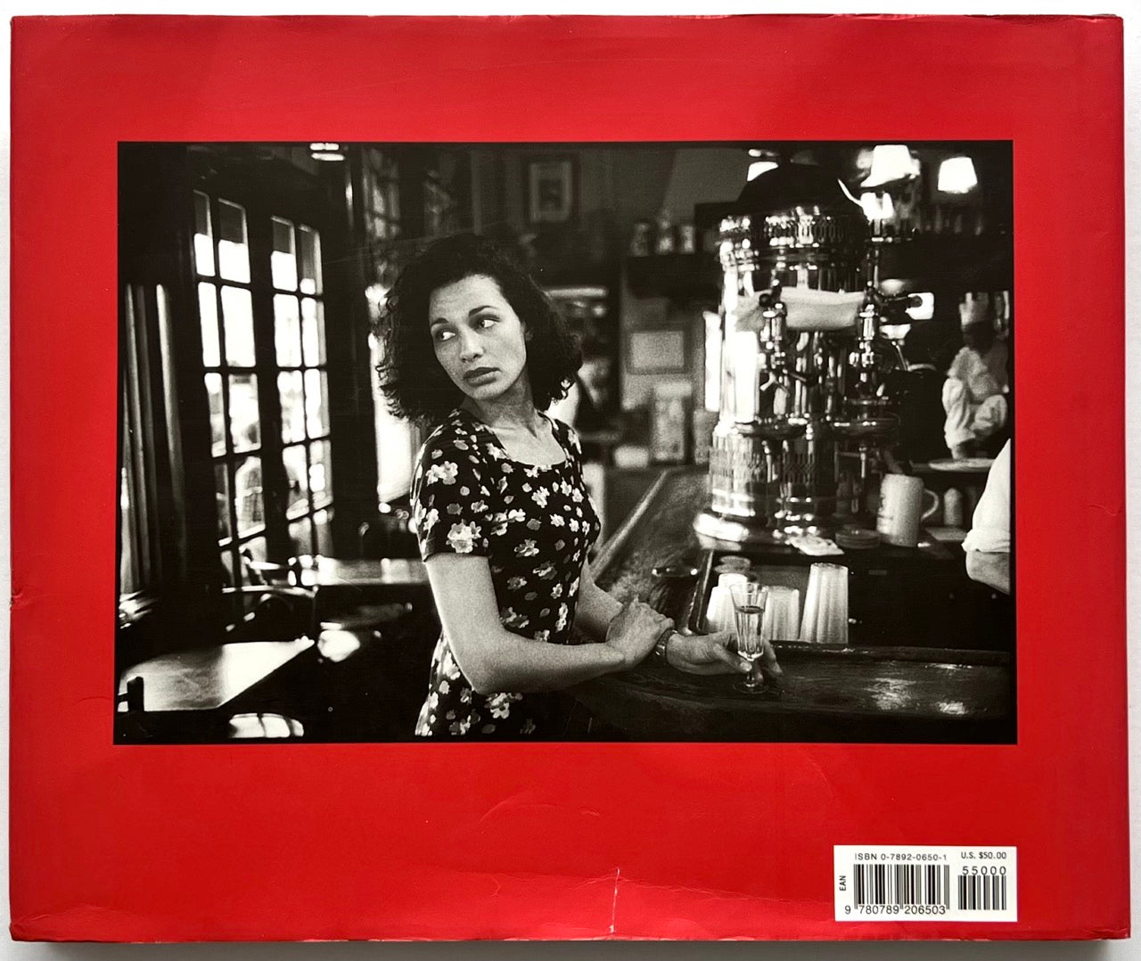 Back cover of Parisians by Peter Turnley, published in 2000, featuring a black-and-white photograph of a woman standing at a Paris café bar, set against a vivid red dust jacket with ISBN barcode in the lower right corner.