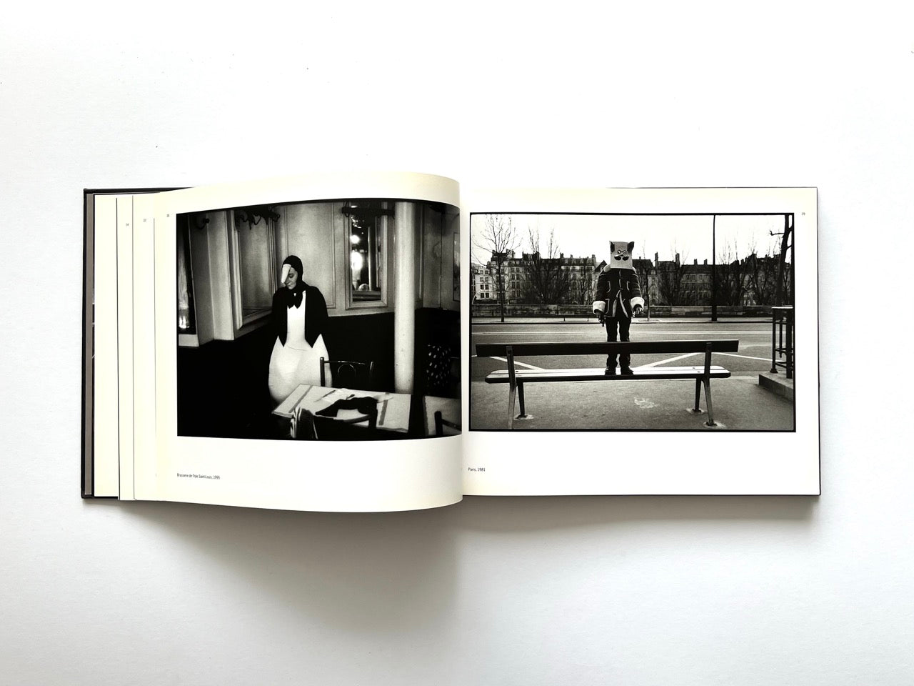 Interior spread from Parisians by Peter Turnley, published in 2000, showing black-and-white photographs of a costumed figure in a Paris café and a person wearing a paper bag mask on a city bench.