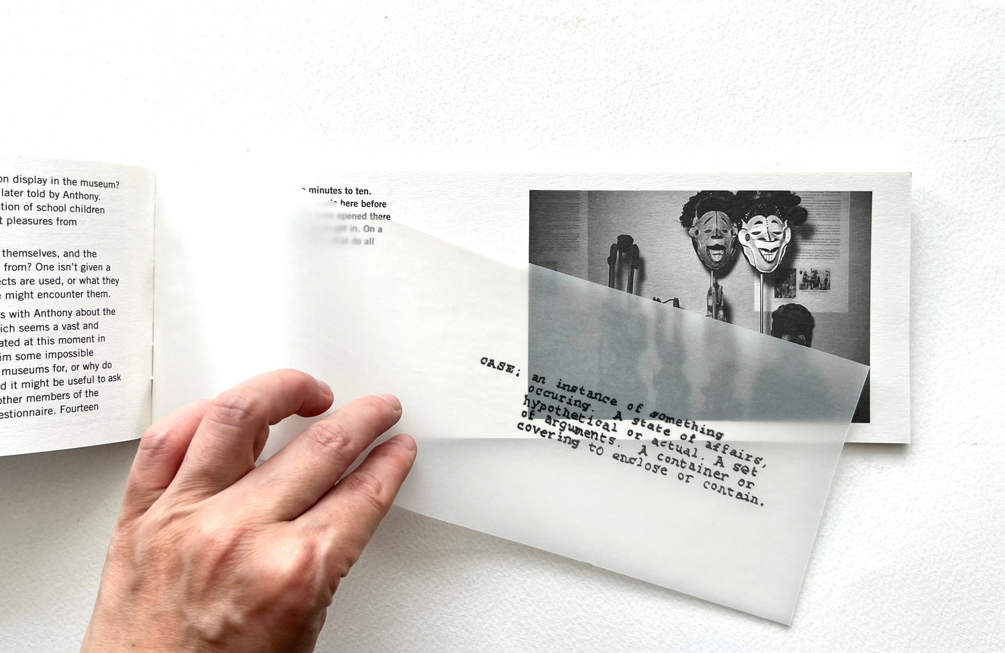 Hand holding a book with text and a black and white photo of a man with a mask on a white background