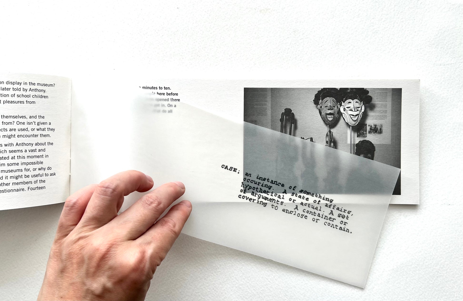Hand holding a book with text and a black and white photo of a man with a mask on a white background