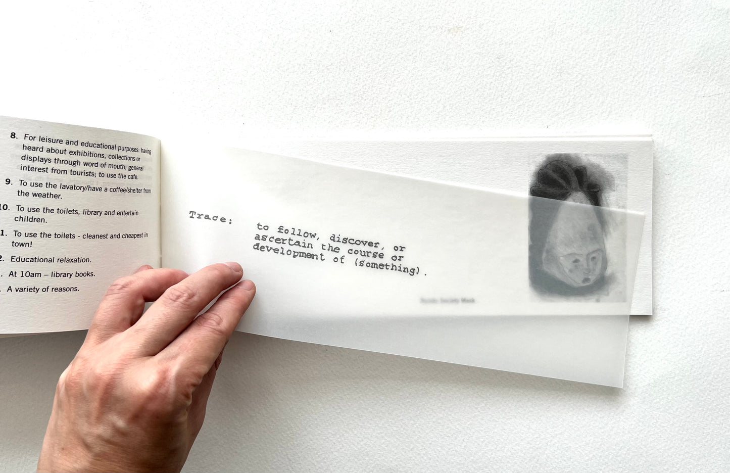 Hand holding an open book with text and a black and white illustration on a white background