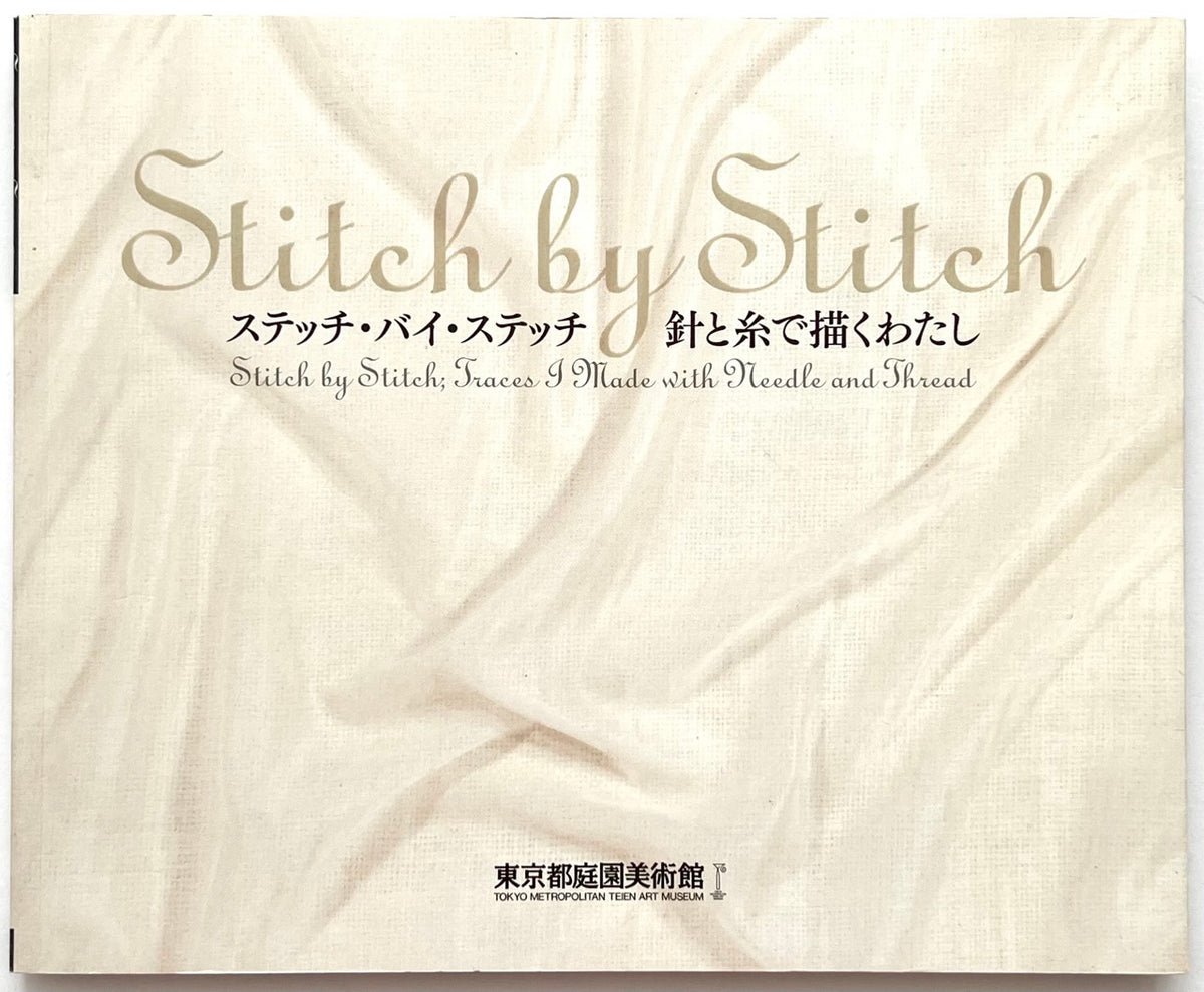 The front cover of the book 'Stitch by Stitch' (ステッチ・バイ・スチュート), featuring elegant gold script and Japanese text printed on a textured, cream-colored fabric background.
