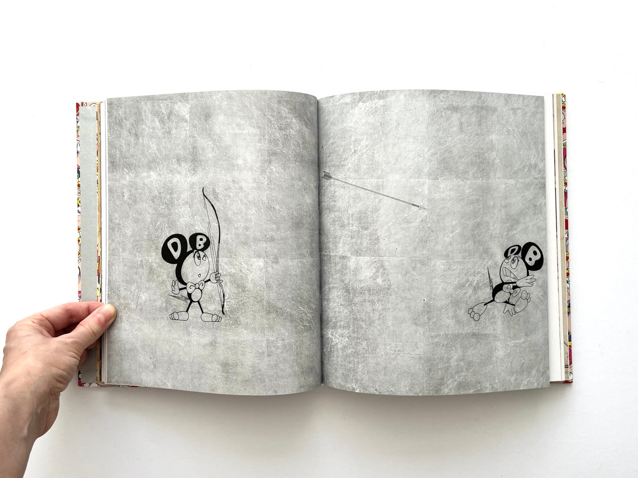 Takashi Murakami Lineage of Eccentrics interior spread showing minimalist cartoon figures with bows and arrows on a textured grey background